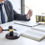 An estate planning lawyer in his office holding a gavel in one hand and glasses in the other.