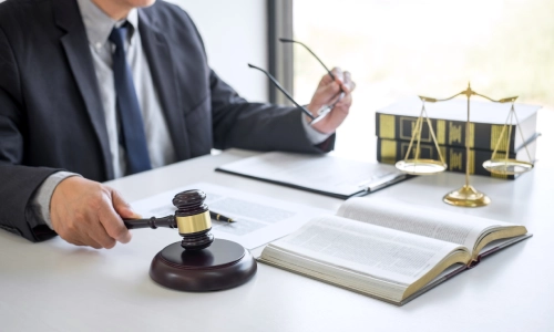 An estate planning lawyer in his office holding a gavel in one hand and glasses in the other.