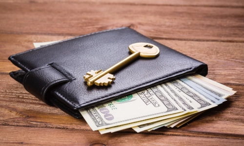 A full wallet resting on a table with a key on top of it representing asset protection.
