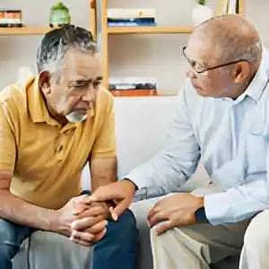 Two older men sitting together, one offering comfort to the other.