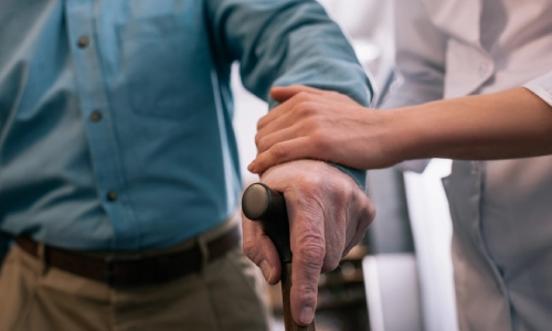Close up of an elderly man recieving assistance from a younger person while walking
