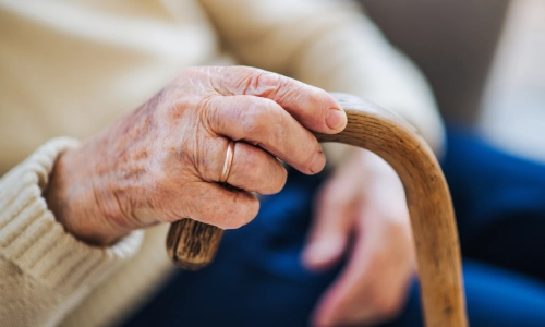 A close-up photo of an elderly woman holding a wooden cane.