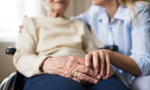 Elderly woman on a wheelchair sitting with a younger woman with her arm around the elder