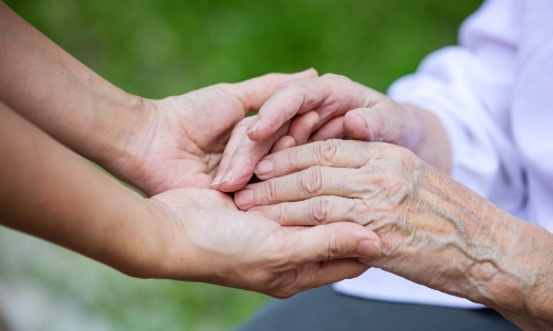 Close up of middle aged womans hand holding an elderly woman's hands in her own