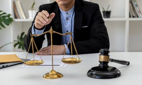 A New Jersey Medicaid planning attorney gestures with a pen in their right hand while sitting behind an office desk with a hammer and scales of justice in the foreground