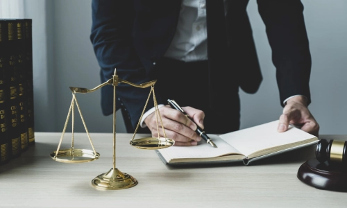 A New Jersey Medicaid planning attorney stands and leans over a desk while writing on a black notebook