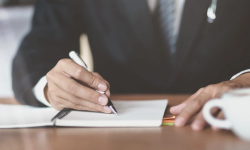 An East Brunswick trusts and estates lawyer takes notes in a white notebook while a coffee mug sits at their left side