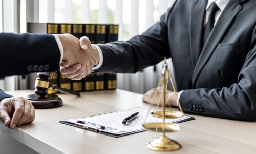 An East Windsor trusts and estates lawyer sits in a law office while shaking the hand of a person sitting across the office desk