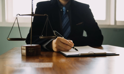 A trusts and estates lawyer serving Flemington signing a document placed on an office desk with balance scales to his right side