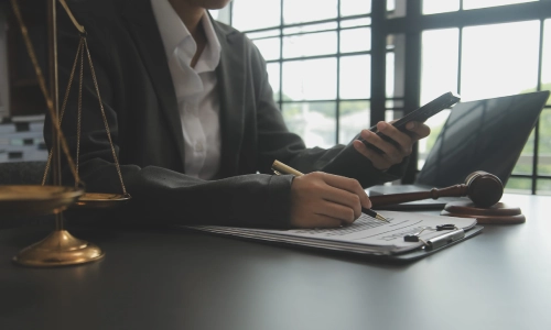 A Florence trusts and estates lawyer working on a laptop while viewing notes on their smart phone while they sit in a law office