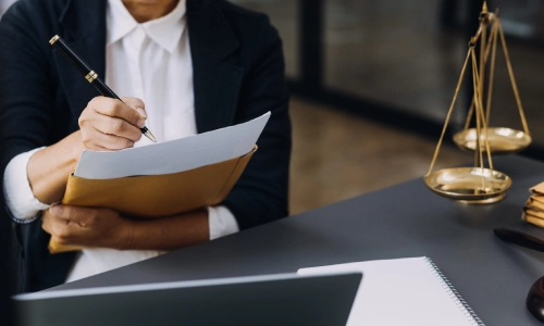 A trusts and estates lawyer serving Hamilton is holding an envelope while signing a document that is partially pulled out of it