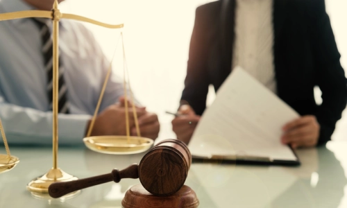 A Hillsborough trusts and estates lawyer is going through legal documents beside a client holding both hands together on top of an office desk