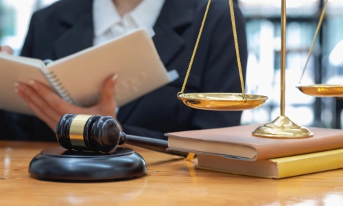 A Middlesex County trusts and estates lawyer reading the contents of a notebook in their hand while sitting at a table with balance scales and a hammer and gavel