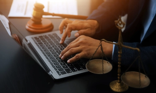 A North Brunswick trusts and estates lawyer is typing on a laptop placed in between a hammer and gavel and balance scales on a table