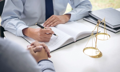 A Plainsboro trusts and estates lawyer writes on a data book while speaking to a client sitting beside an office desk
