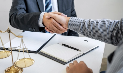A trenton trusts and estates lawyer shakes the hand of a client with a signed contract placed on the office table beside an open notebook