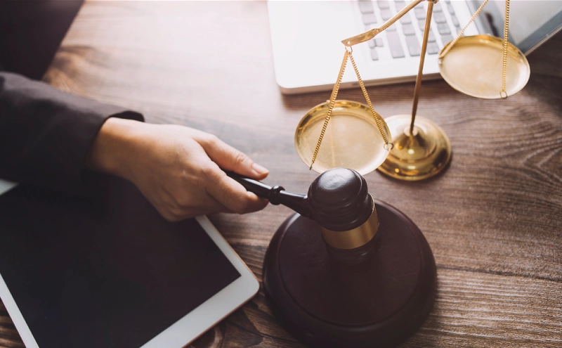 A wills and trusts attorney holding a gavel over its soundblock next to a tablet and scales on a desk.