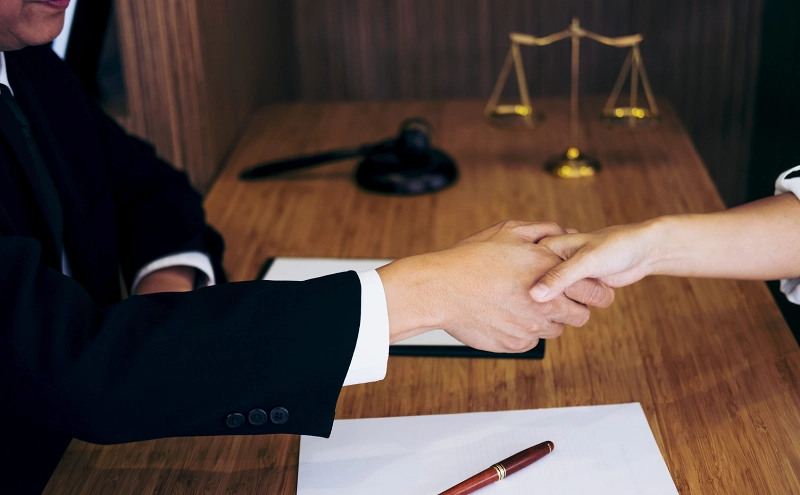 An estate planning lawyer sits at an office desk while shaking hands with a satisfied client