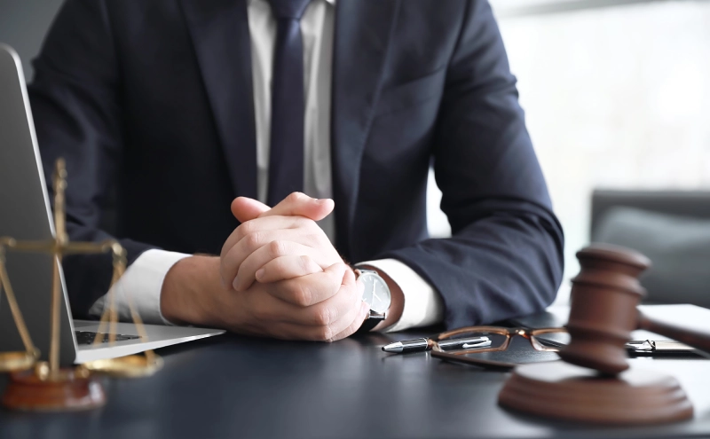 An elder law attorney waiting for a client patiently from behind his desk with his hands clasped.